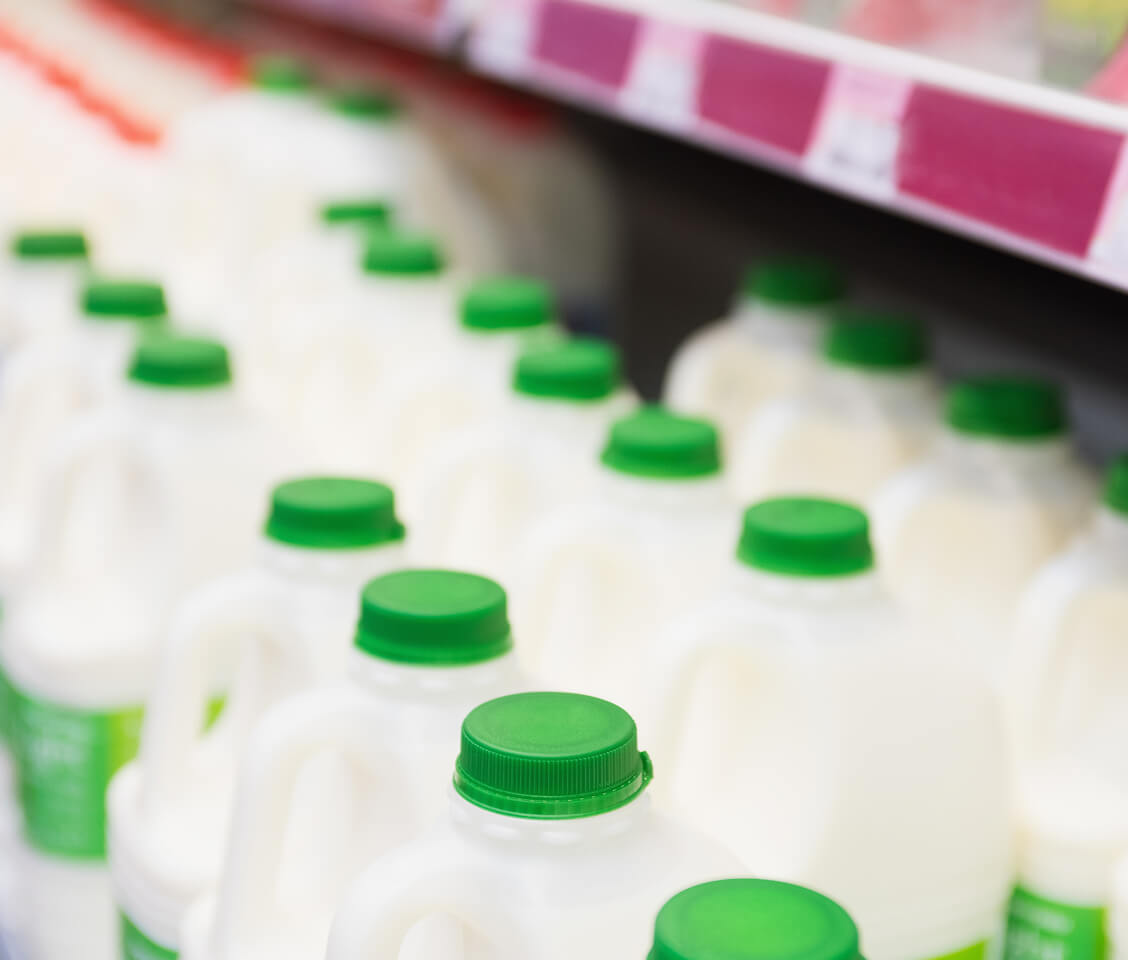 Rows of white plastic milk jugs with green caps on a grocery store shelf.