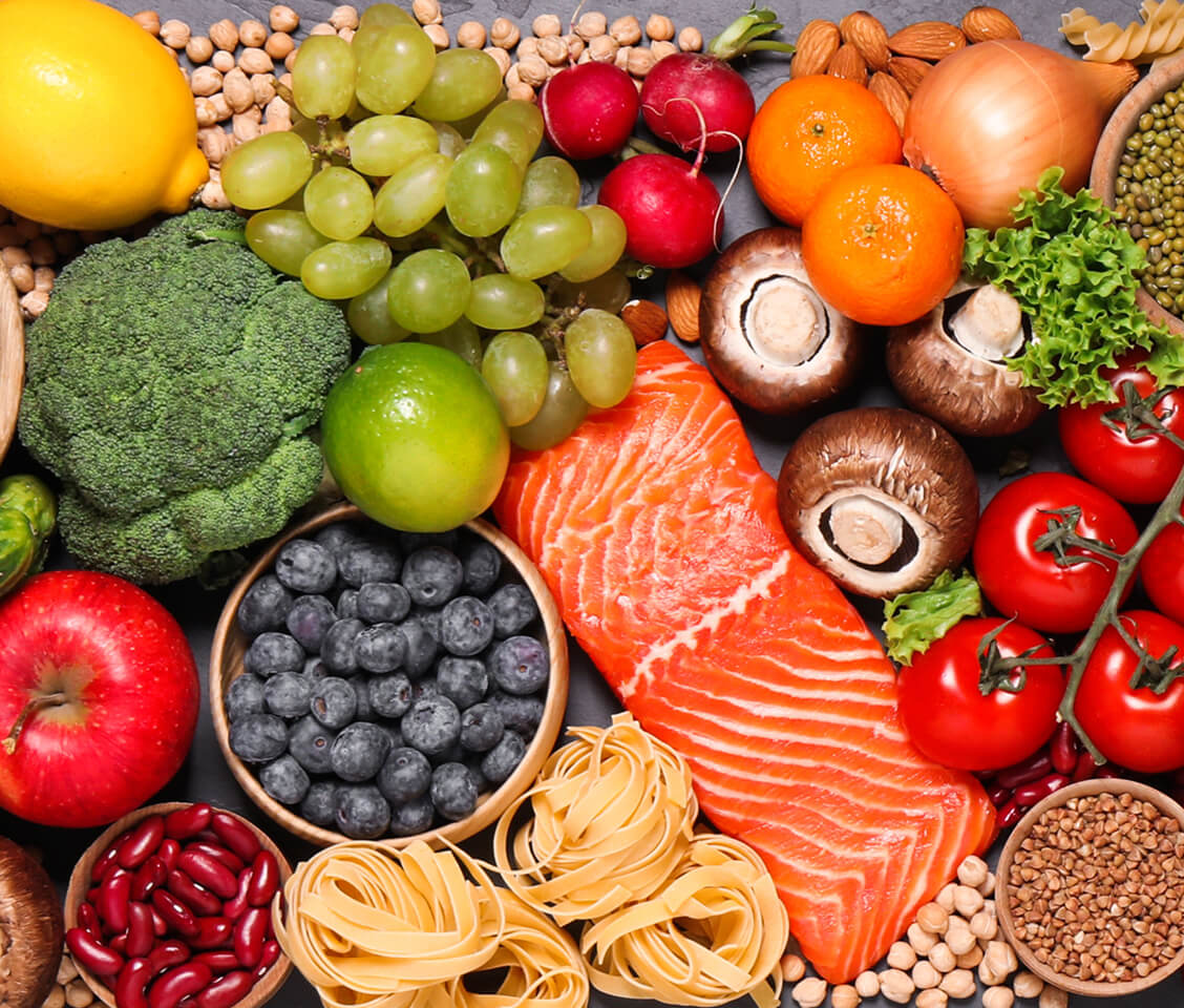 Healthy foods including salmon, broccoli, grapes, tomatoes, blueberries, nuts, apples, and pasta.