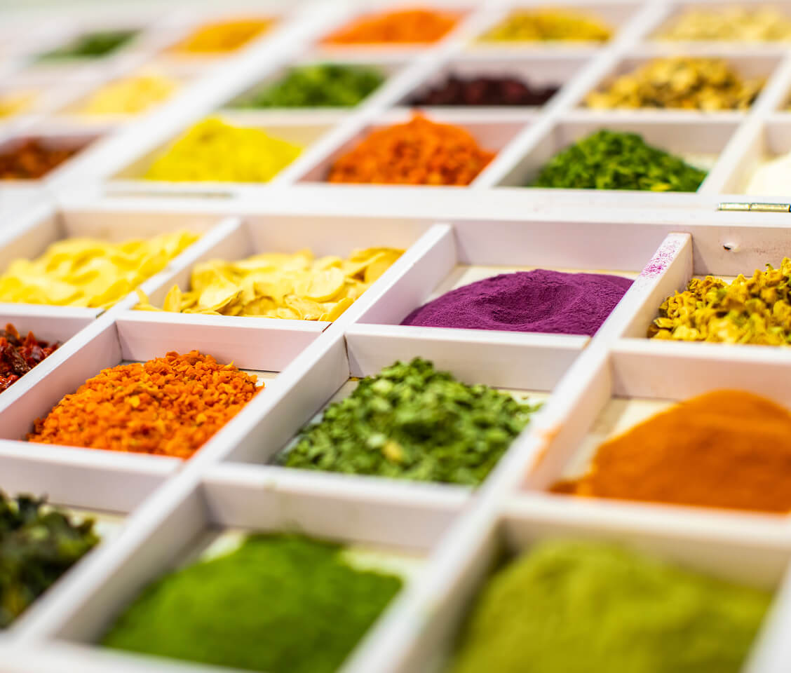 Close-up of a white wooden spice box with compartments holding colorful powdered and dried spices.
