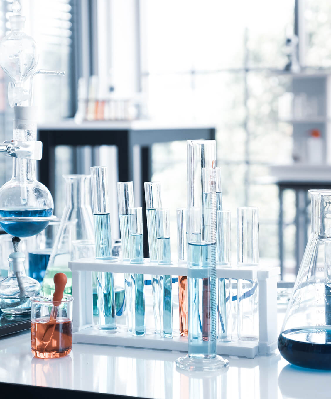 Test tubes and beakers with blue and orange liquids on a lab bench in a bright laboratory.