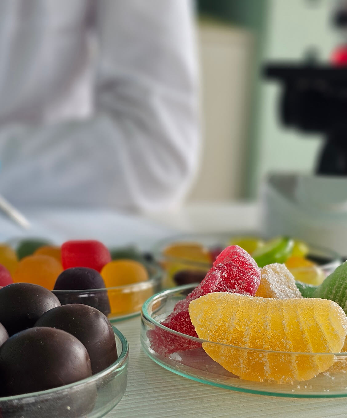 Close-up of assorted colorful sugar-coated gummy candies and dark chocolate balls in glass dishes.
