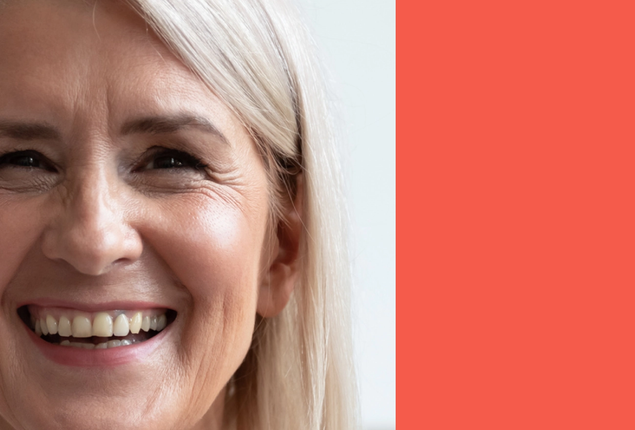 Older woman with white hair smiling next to coral red background, split composition design