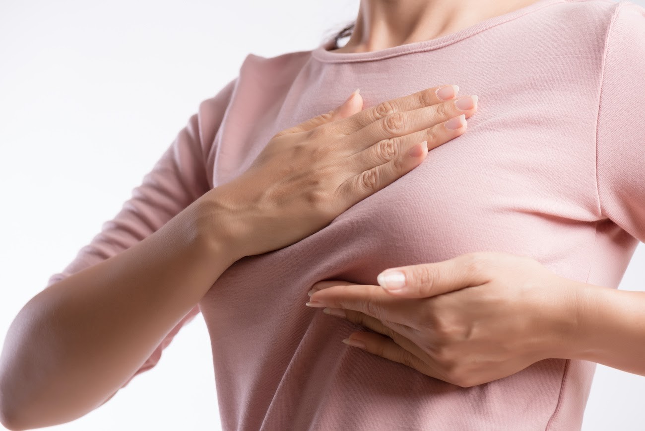 Person in pink long-sleeved shirt with both hands placed on chest area against white background