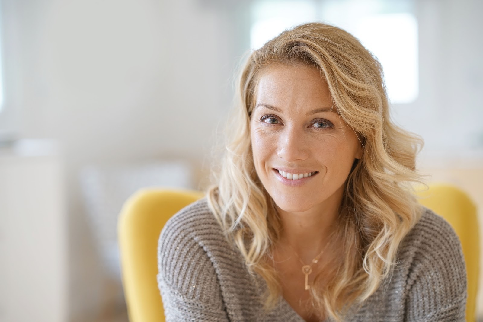 Smiling woman with blonde hair wearing a knitted gray sweater