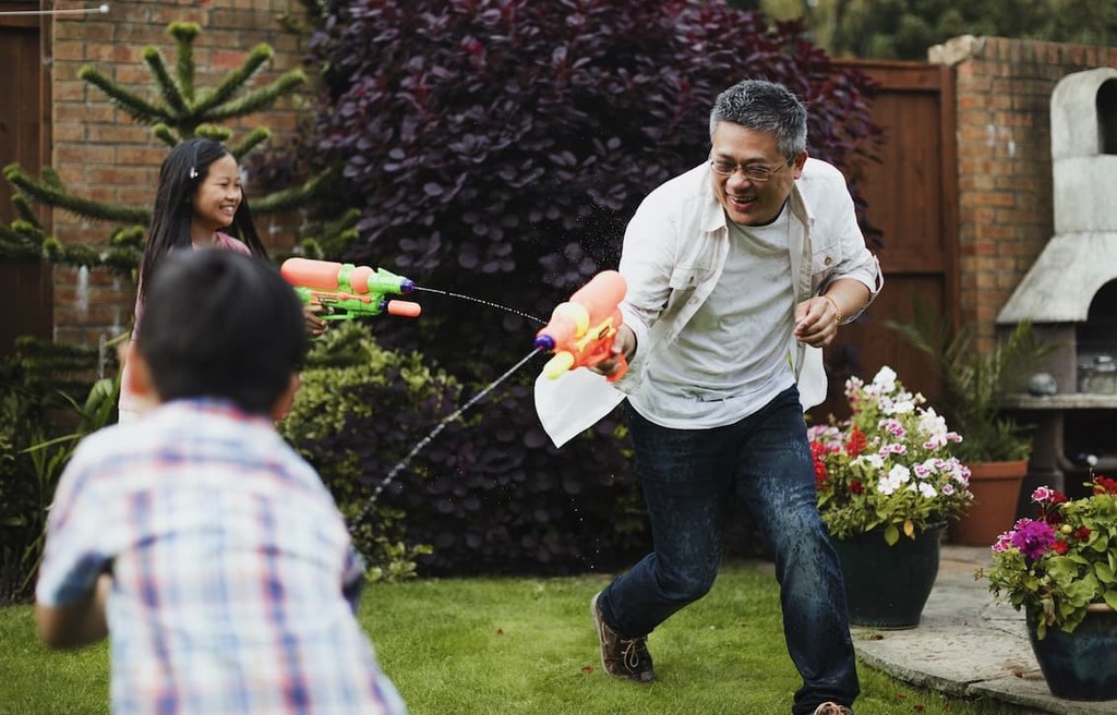 Father playing water gun fight with two children in a backyard garden