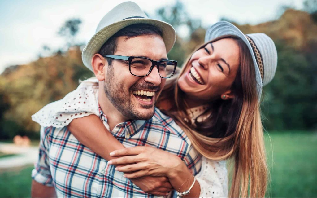 Happy couple laughing together outdoors wearing hats and plaid shirt in scenic nature setting