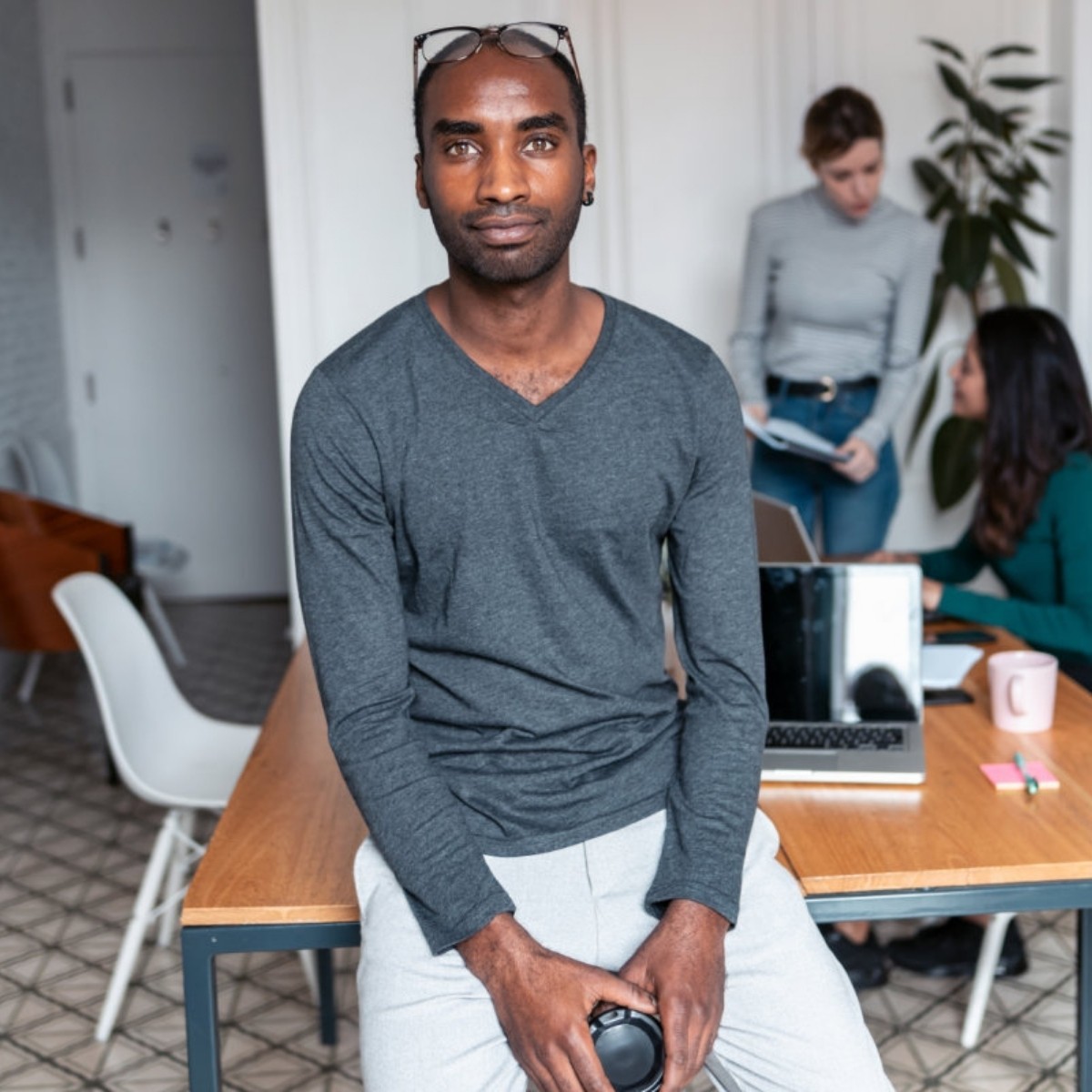 Man in gray shirt sitting at desk with colleagues working in background office space