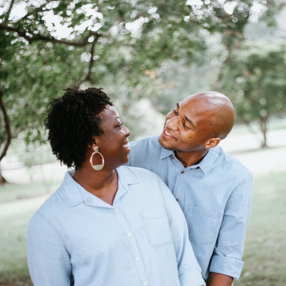 Couple in matching light blue denim shirts smiling together under white flowering tree branches