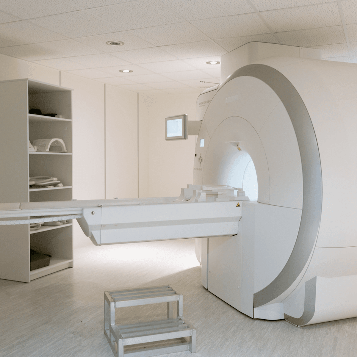 Medical imaging room with white MRI scanning machine, storage shelves, and step stool