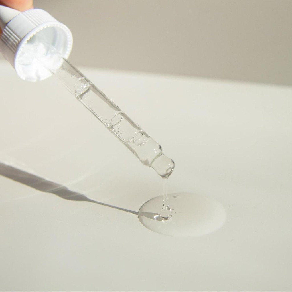 Clear liquid serum being dripped from a dropper onto white surface for cosmetic or medical product testing