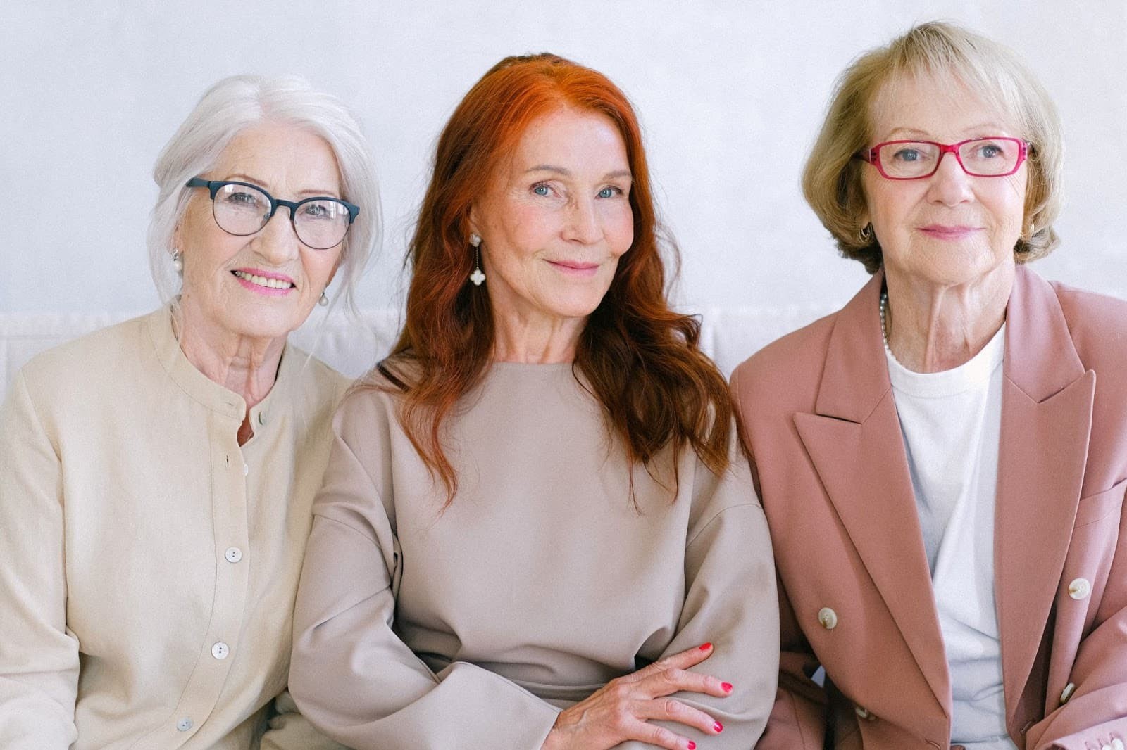 Three mature women smiling together against white background in casual professional attire