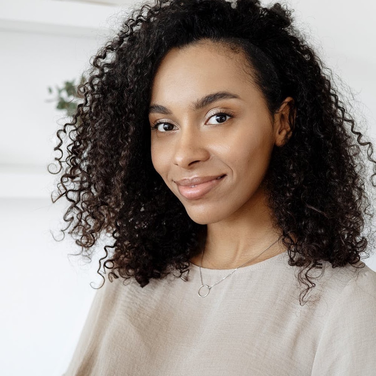 Woman with curly dark hair wearing beige top, smiling at camera against white background