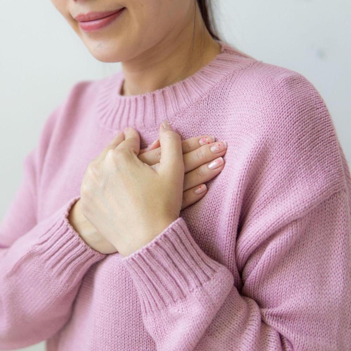 Woman in pink sweater holding hand to chest area, indicating heartburn or chest discomfort