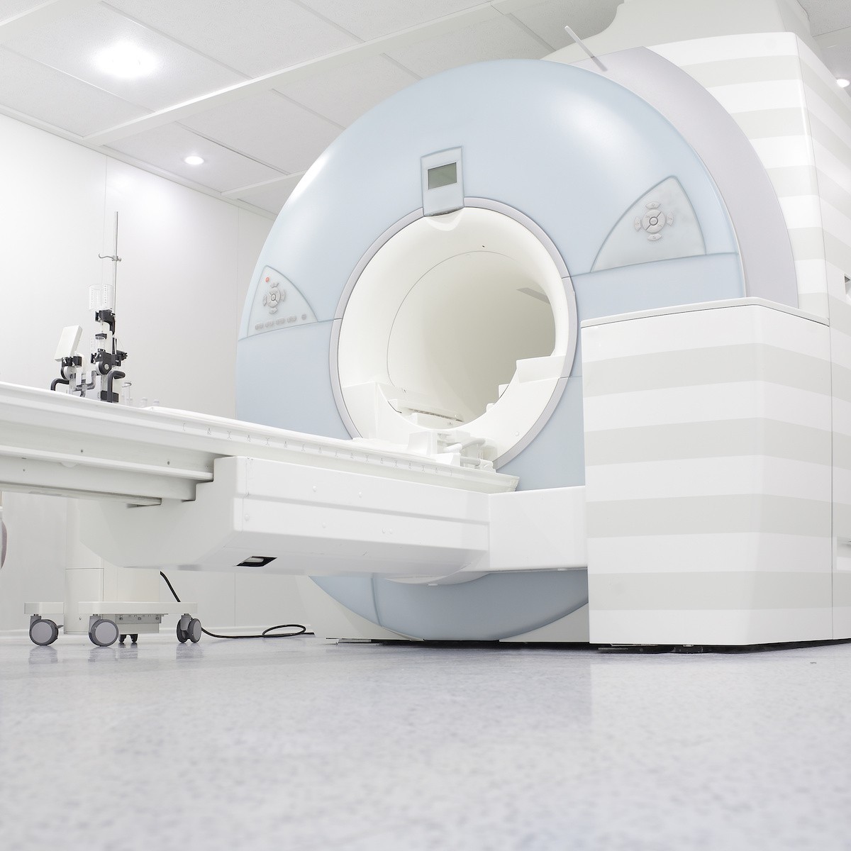 Large white and blue MRI scanner in modern hospital room with cylindrical opening and control equipment on left