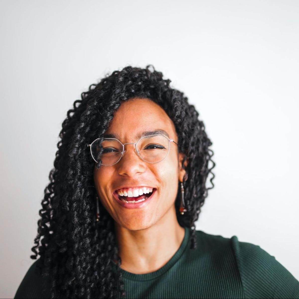 Smiling person with long braids wearing glasses and green sweater against white background