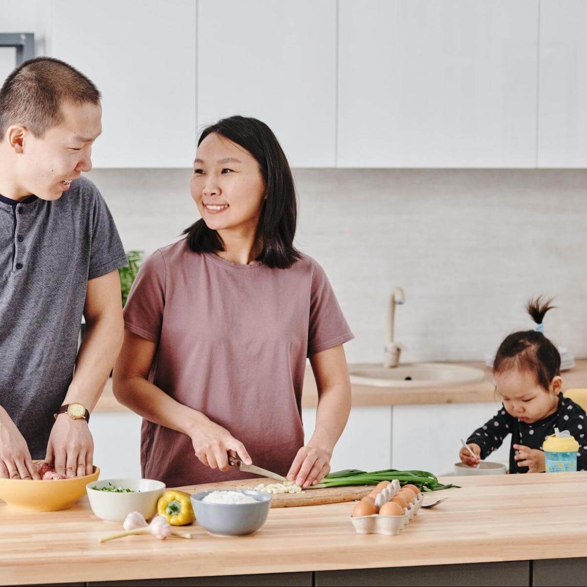 Woman with boy and toddler cooking together at wooden kitchen counter with fresh ingredients