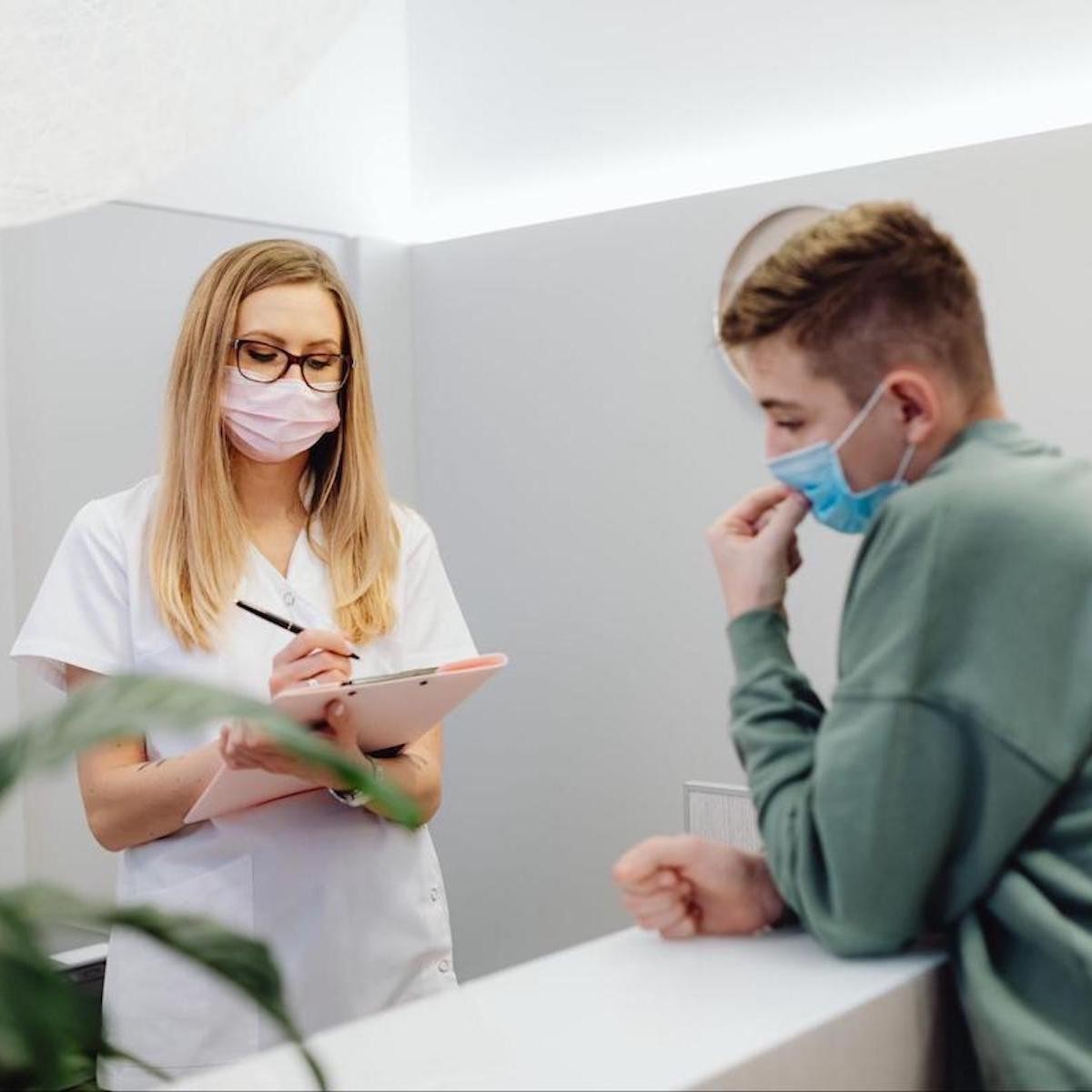 Female healthcare worker in mask consulting with young patient in medical office clinic setting