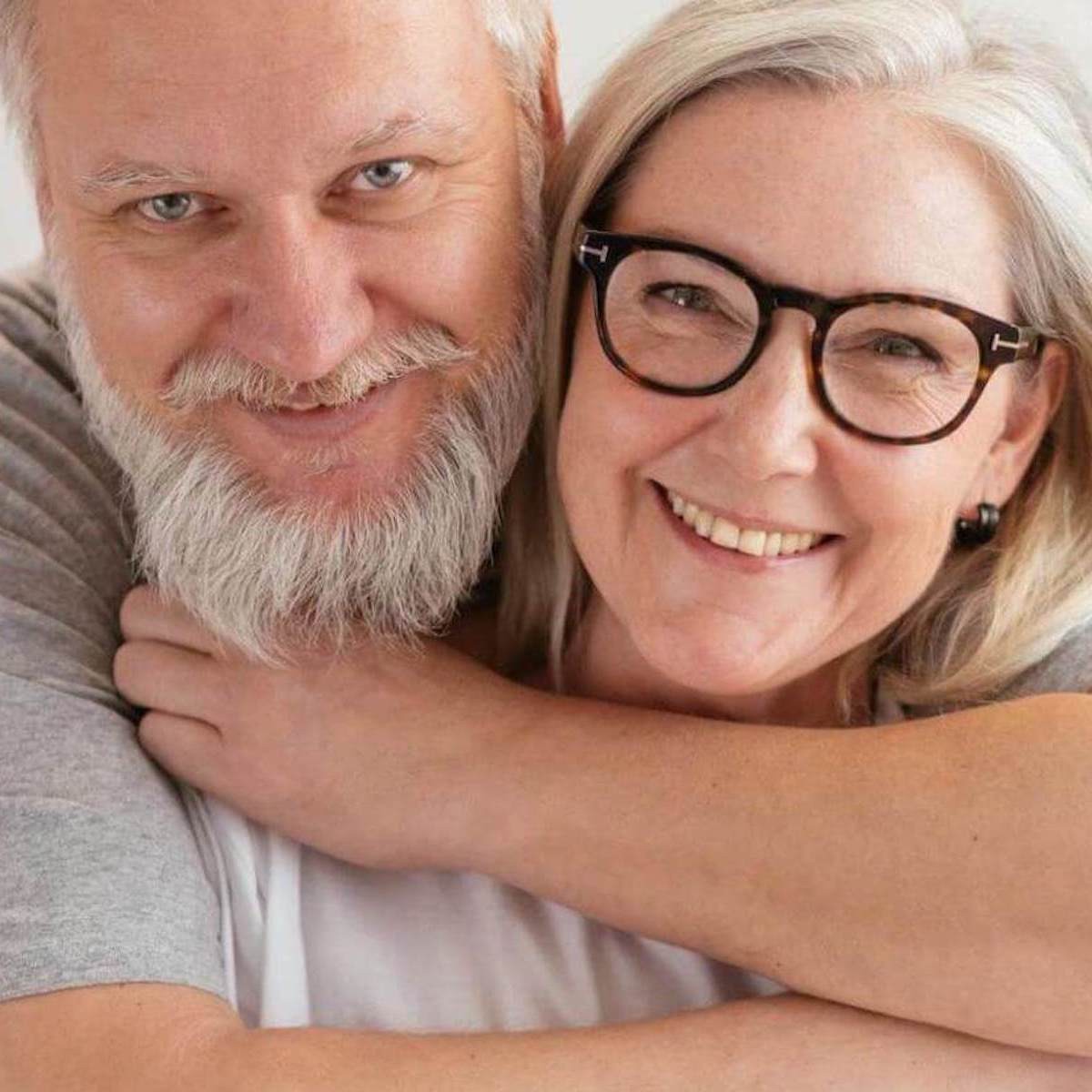 Smiling senior couple embracing in close portrait pose against white background