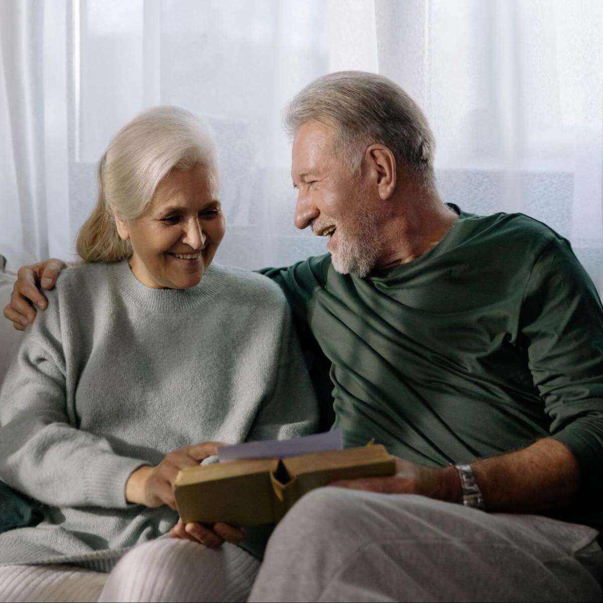 Senior couple smiling together while reading a book indoors with natural window light