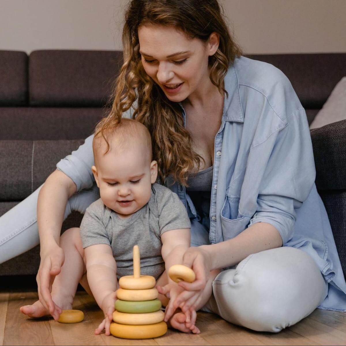 Mother and toddler playing with stacking rings toy on floor indoors by couch