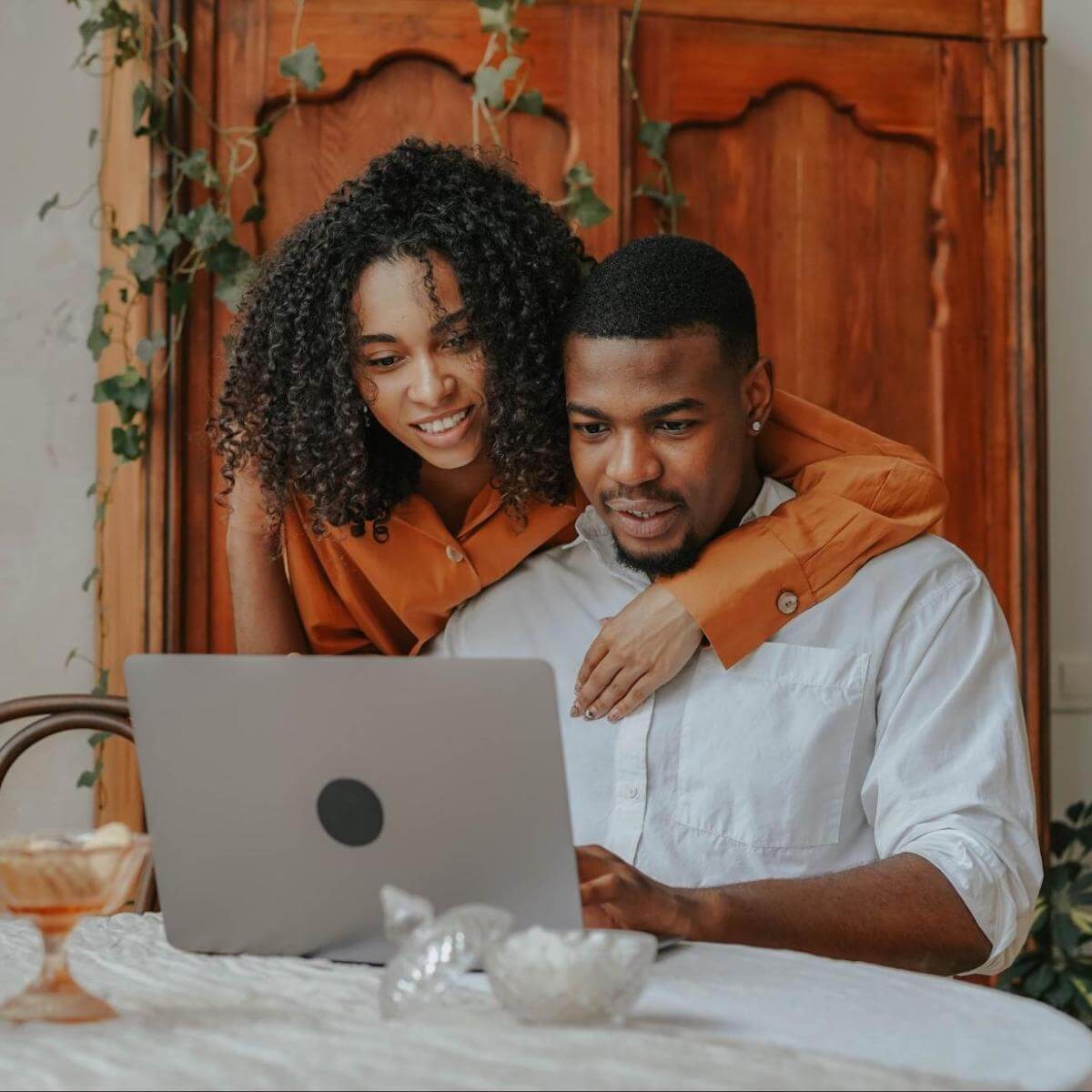 Young couple smiling while viewing laptop together at table with wooden door background