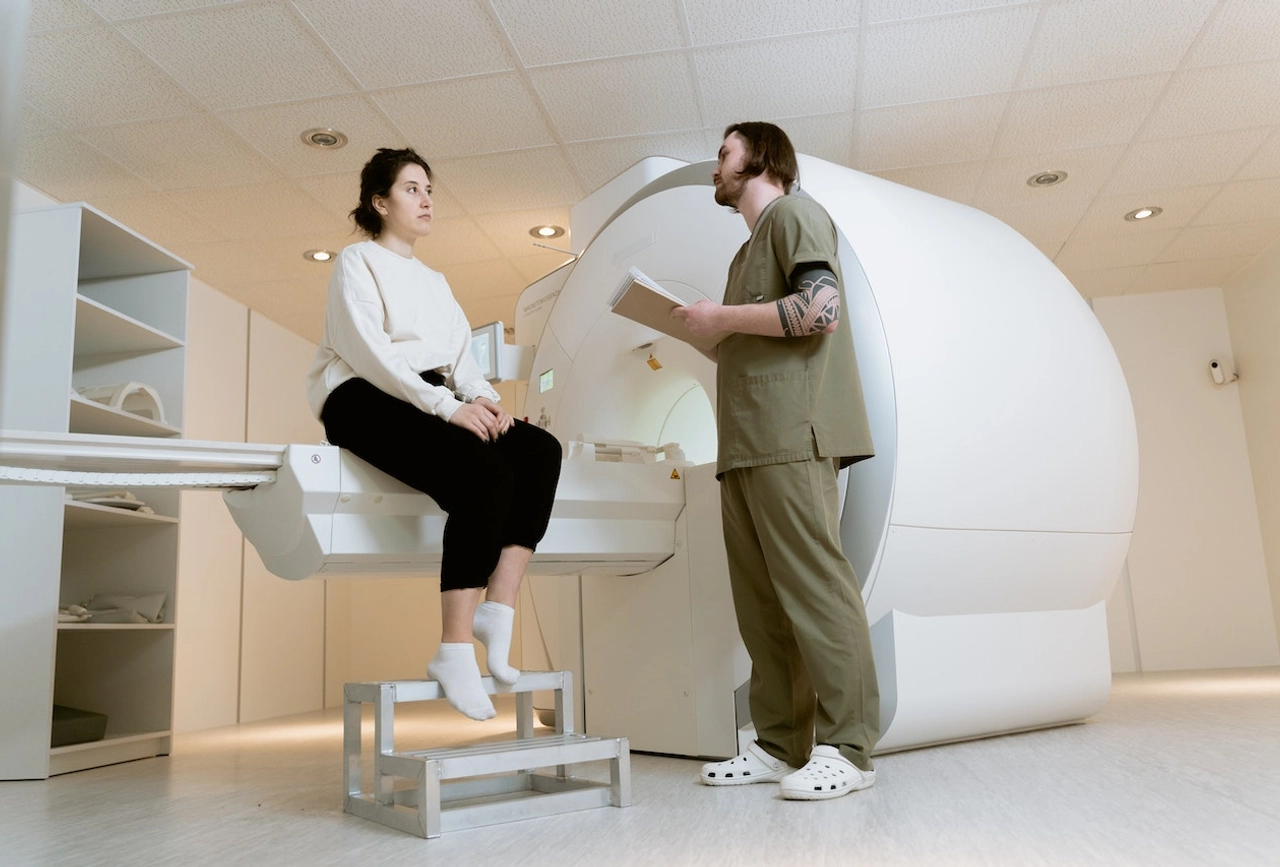 Medical technician with clipboard consulting patient positioned inside MRI scanning machine in hospital
