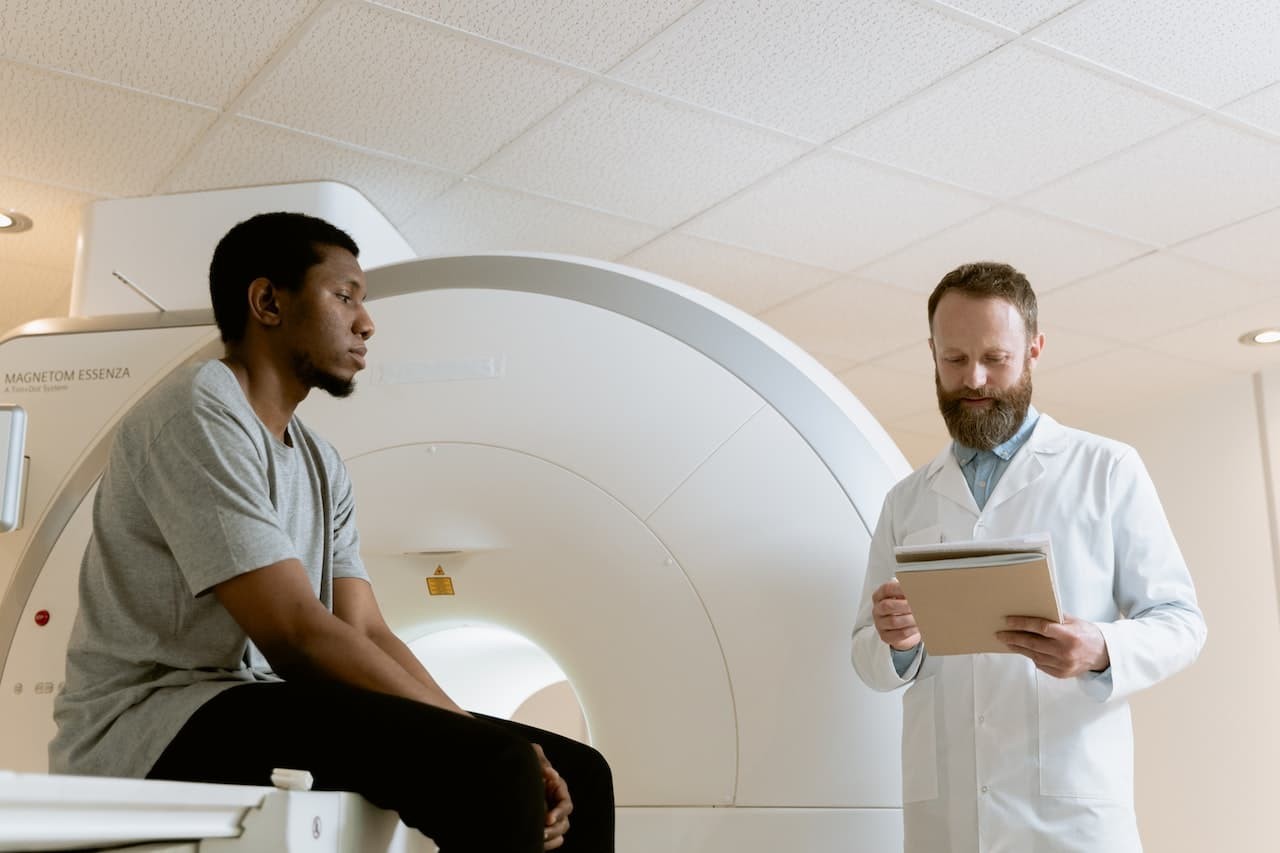 Doctor in white coat with tablet consulting patient beside MRI scanning machine in hospital