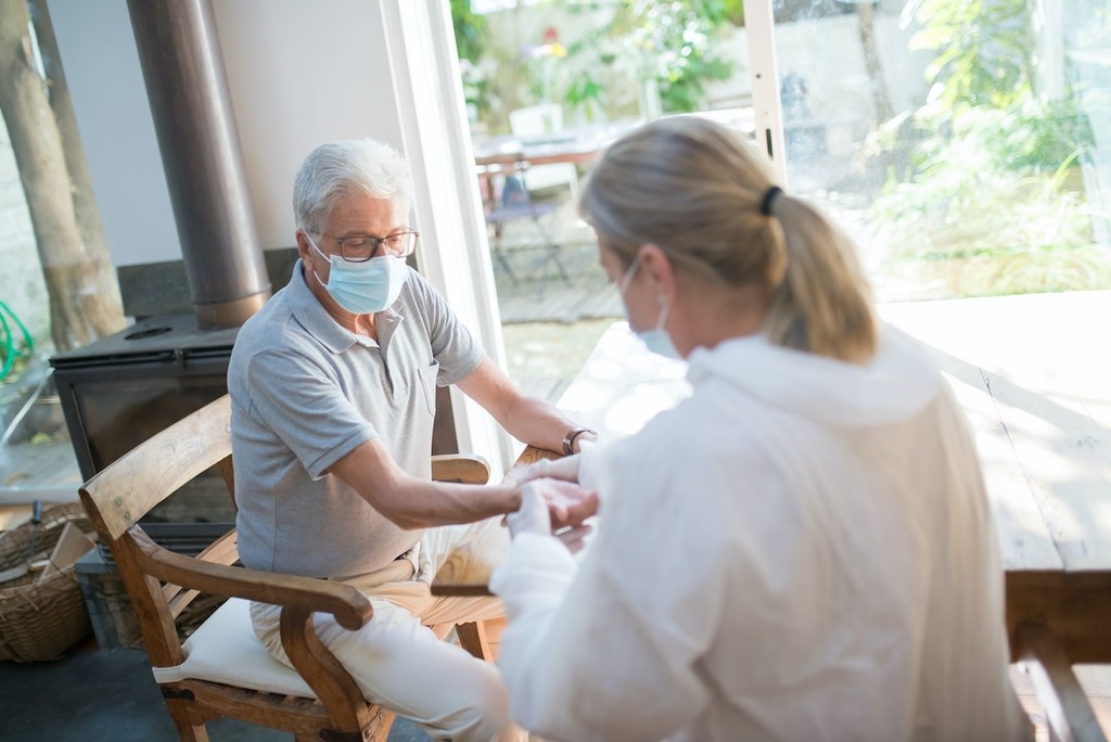 Older man in glasses and mask speaking with woman in white by home fireplace