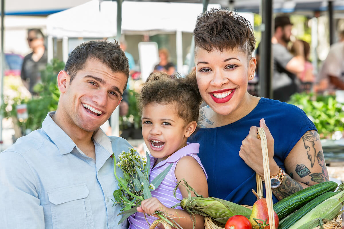 Happy family of three smiling while shopping for fresh produce at a farmers market