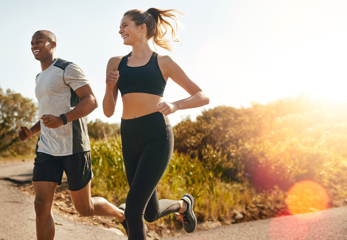 Happy couple jogging together on scenic road during golden sunset with trees in background