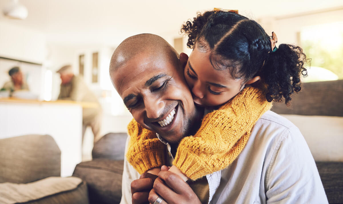 Father laughing while holding daughter in yellow sweater in bright family home living room