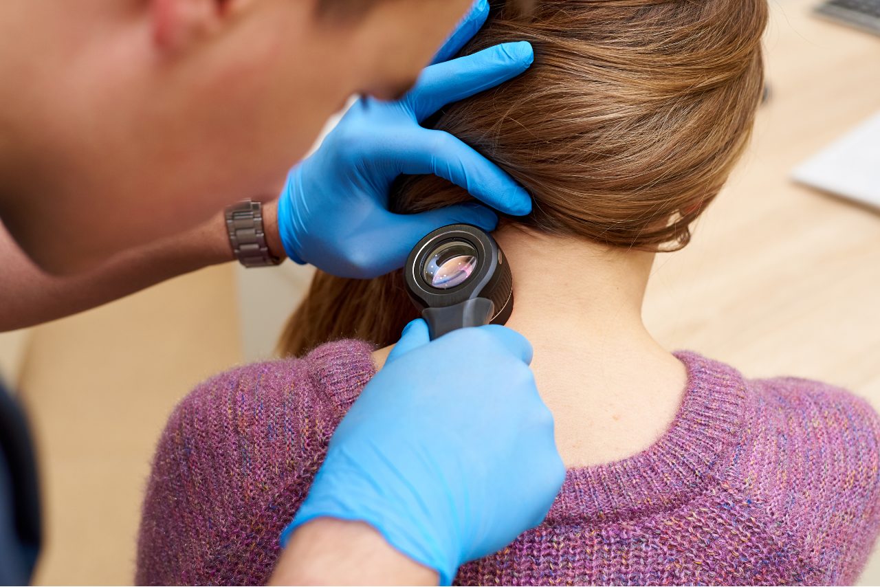 Doctor in blue gloves using dermatoscope to examine patient's neck skin