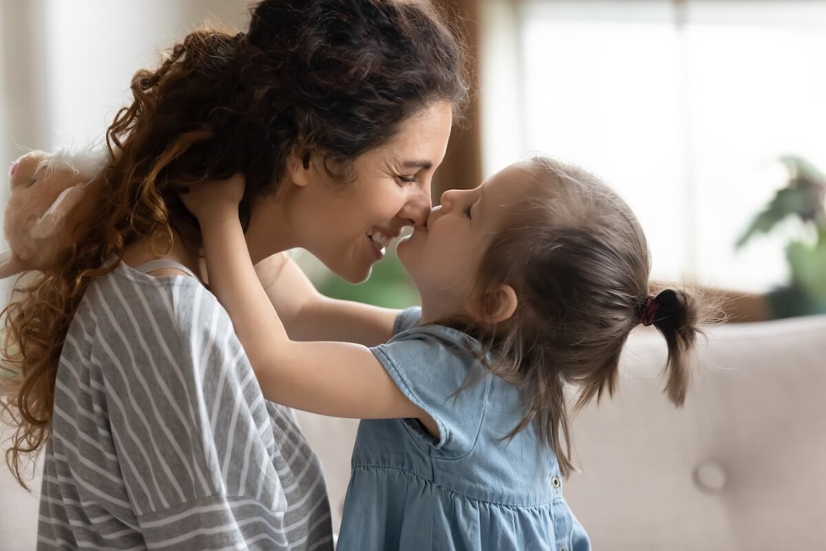 Mother and young daughter face-to-face, smiling affectionately at each other in a warm indoor embrace