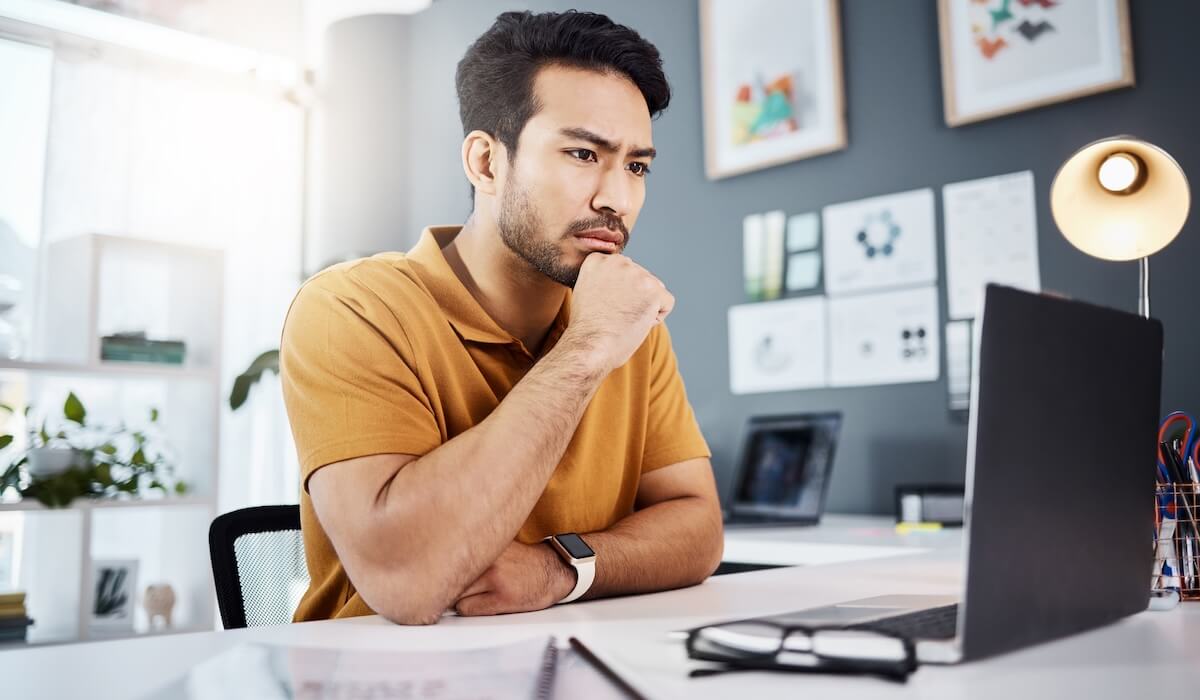 Person in mustard polo looking focused at laptop, modern office with gray wall gallery and smartwatch on wrist.