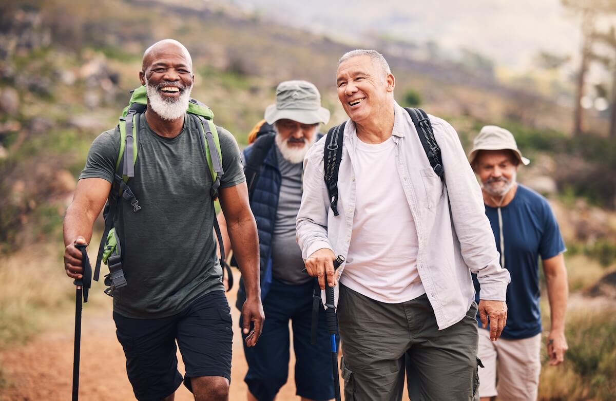 Group of smiling men hiking on mountain trail with backpacks and trekking poles