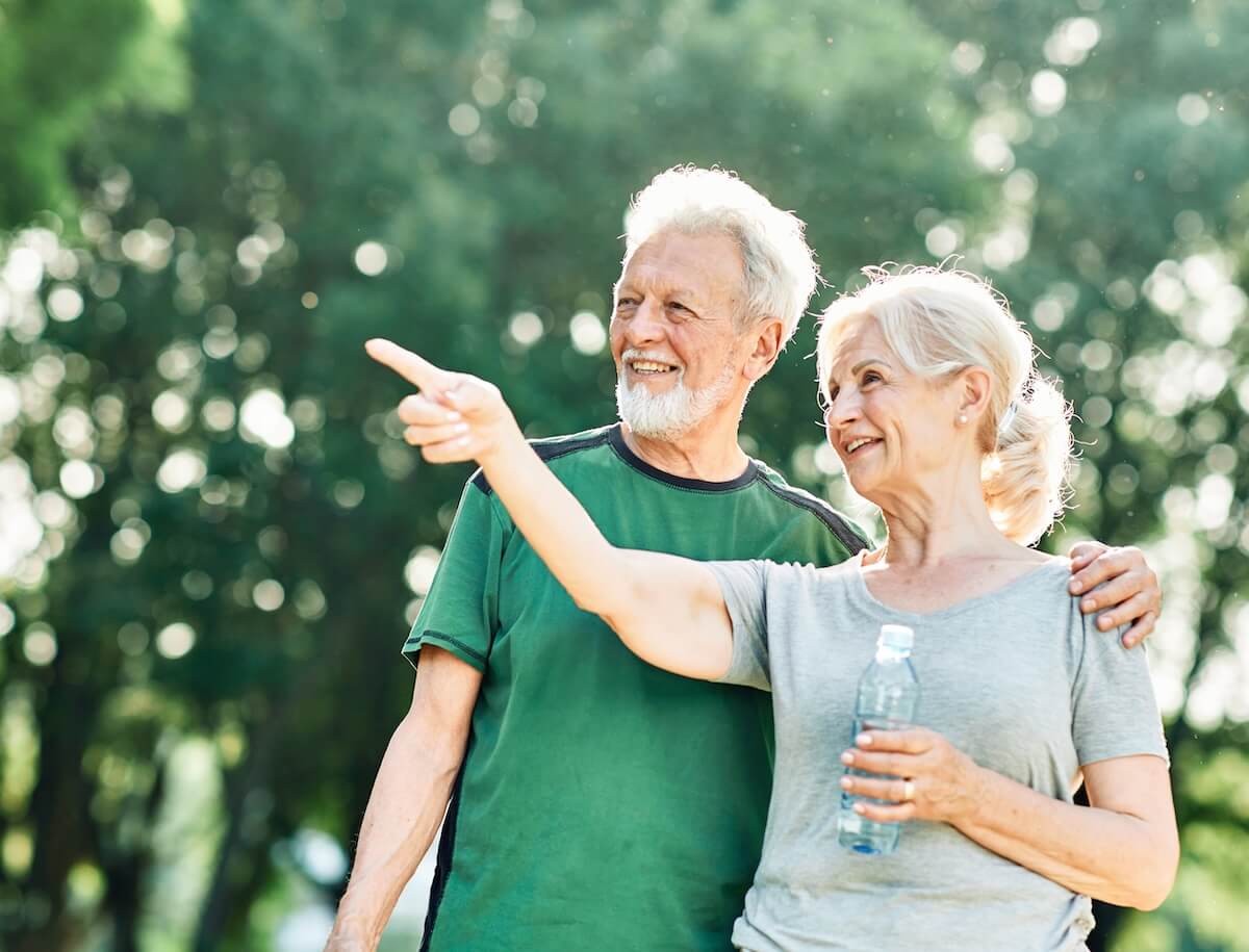 Senior couple outdoors enjoying nature, one pointing at something while the other holds a water bottle