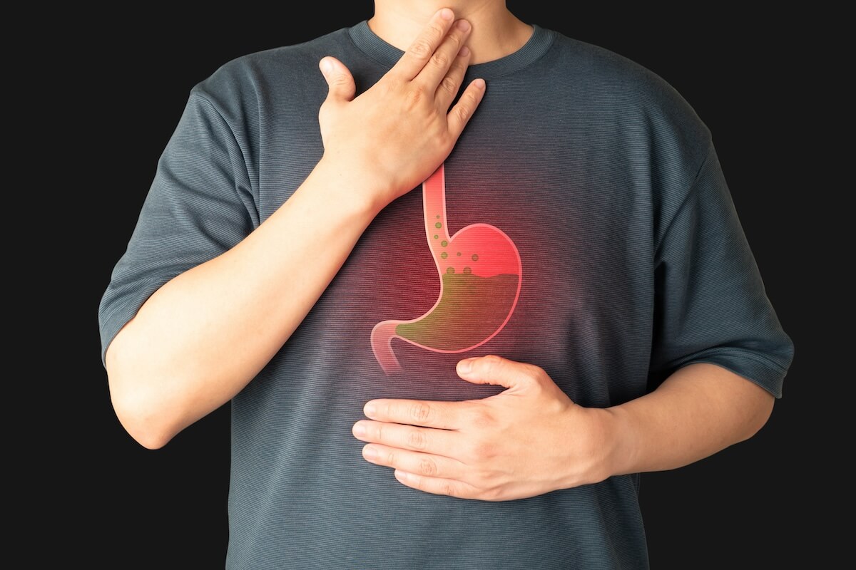 Person touching throat and chest, wearing shirt with stomach illustration showing acid reflux or heartburn