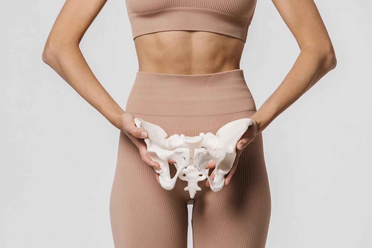 Person in athletic wear holding white pelvic bone model against their lower torso, demonstrating anatomical placement