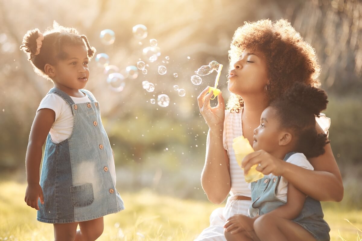 Family enjoying bubbles in golden sunlight, wearing denim and light clothing in a grassy outdoor setting