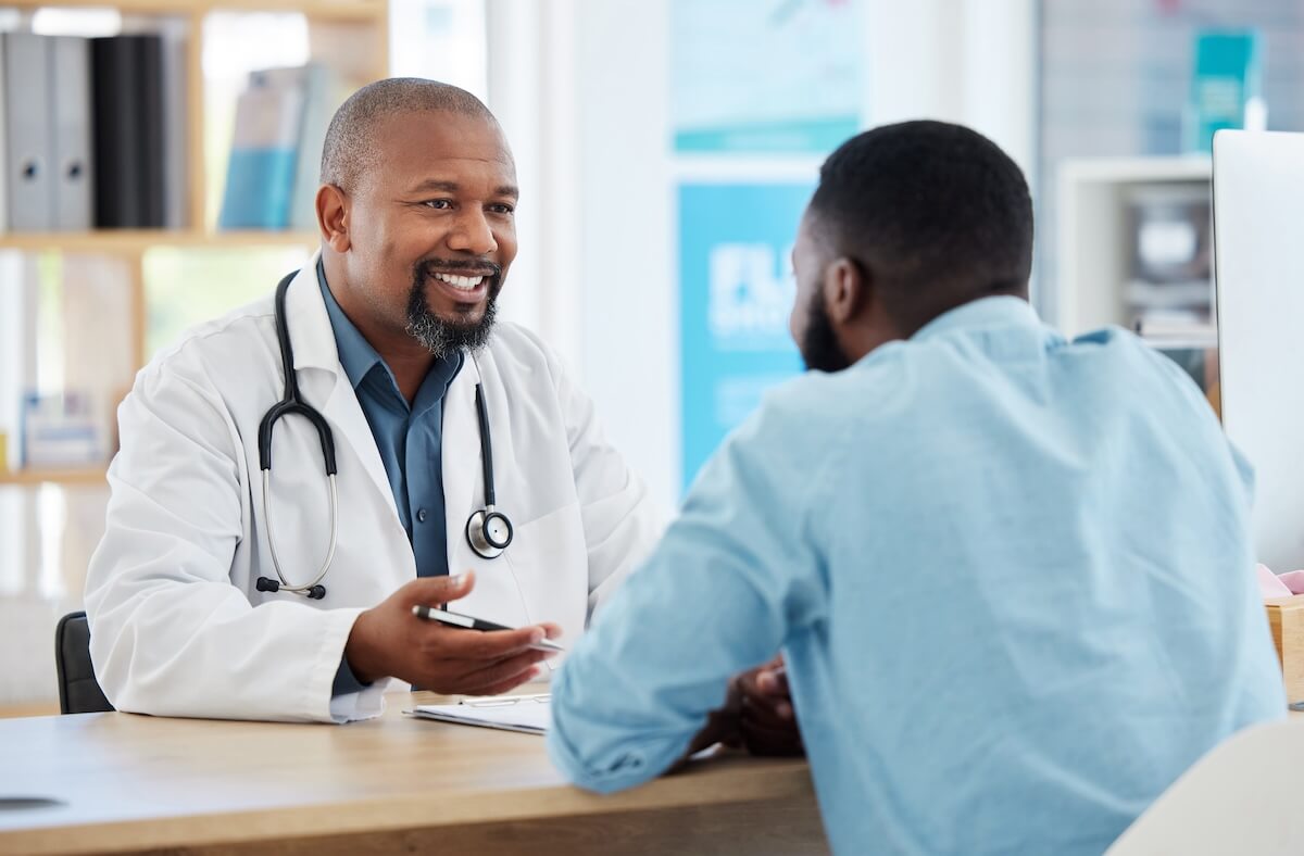 Doctor with stethoscope in white coat speaking with patient during consultation in medical office with bookshelves in background