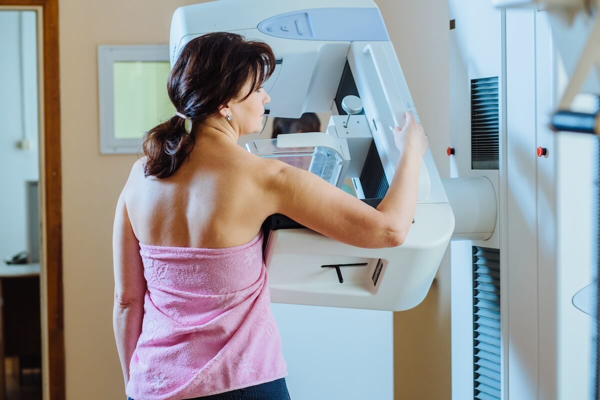 Person in pink wrap positioned at mammography machine for breast cancer screening in medical facility