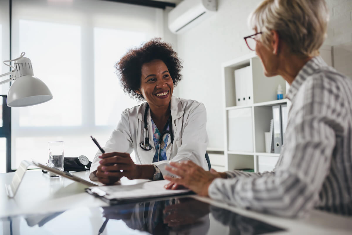Female doctor smiling at senior patient during consultation in bright modern medical office