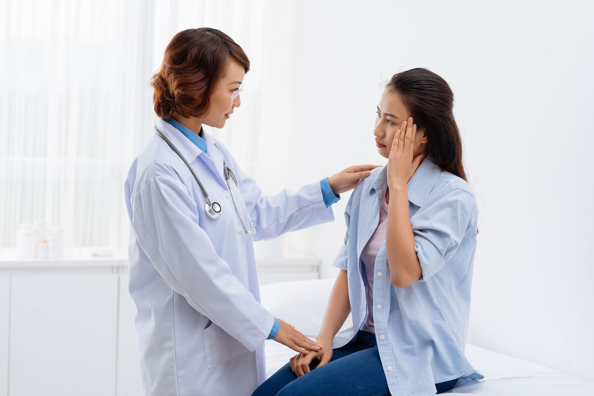 Female doctor examining patient's jaw during physical consultation in bright medical office