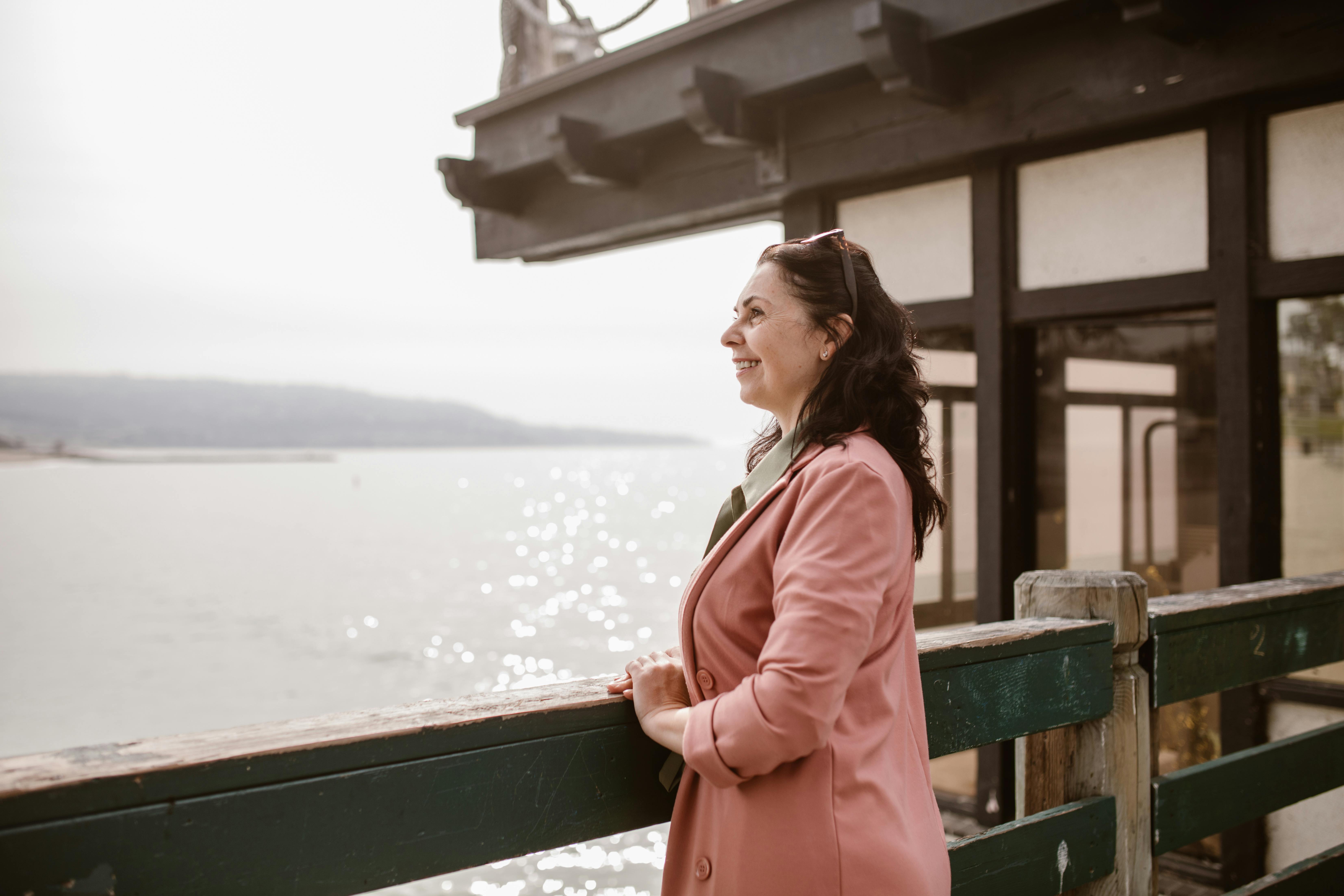 Woman in pink jacket smiling while overlooking water from waterfront deck