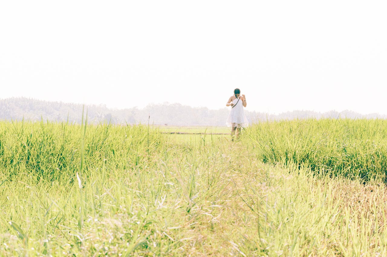 Woman in white dress running through expansive green field with misty mountains in background