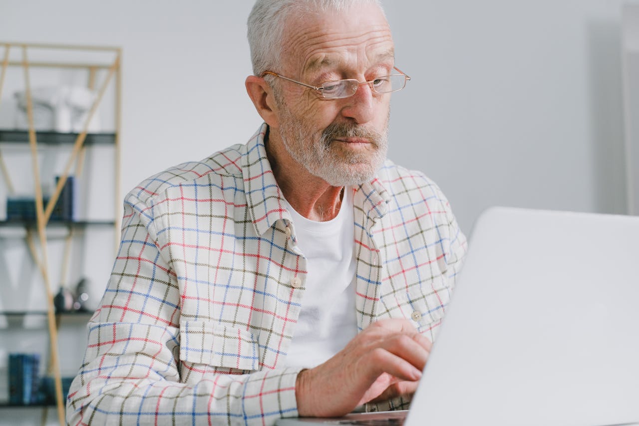 Older man with white beard and glasses working on laptop in modern home office