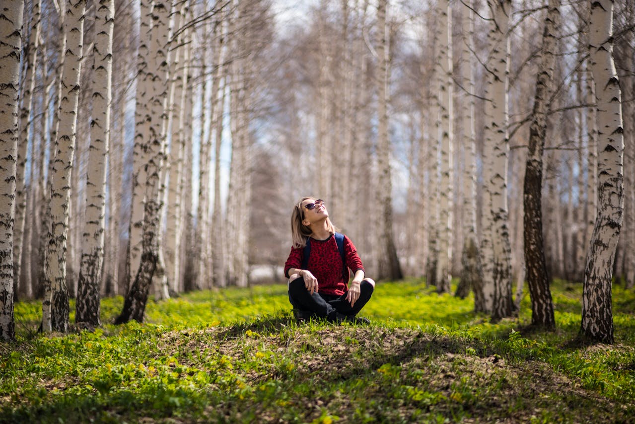 Woman in red top sitting on moss-covered ground in birch forest lined with white and black trees