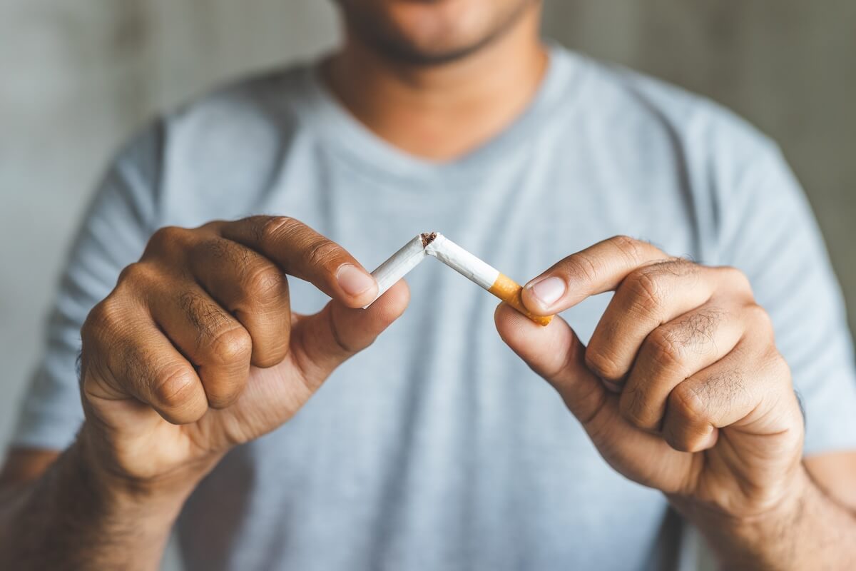 Hands breaking a cigarette in half against light blue shirt background, symbolizing quitting smoking