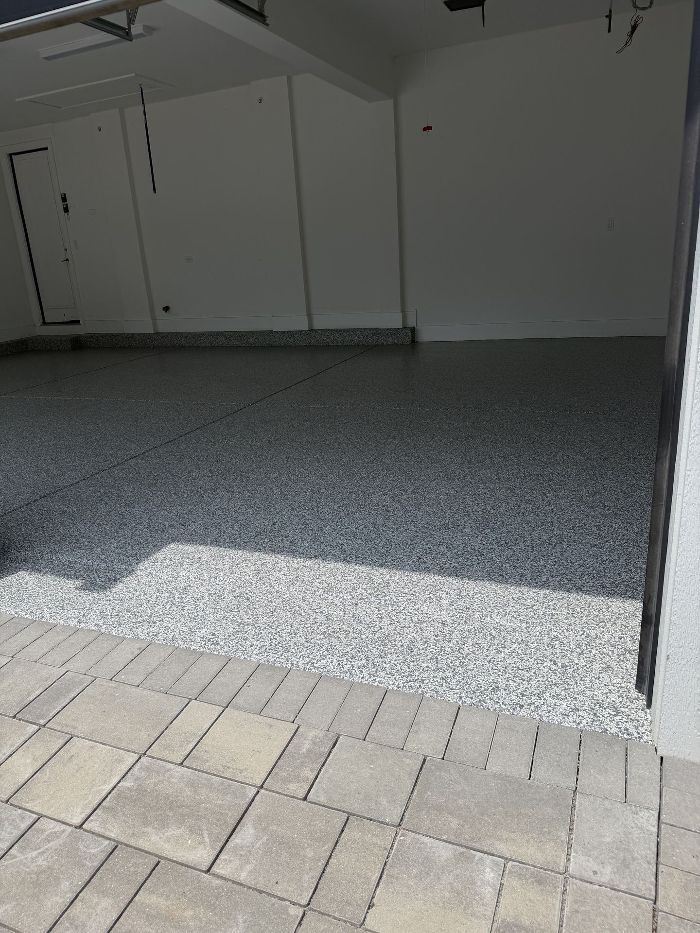 Clean garage with newly installed speckled epoxy floor and gray tiled driveway outside.