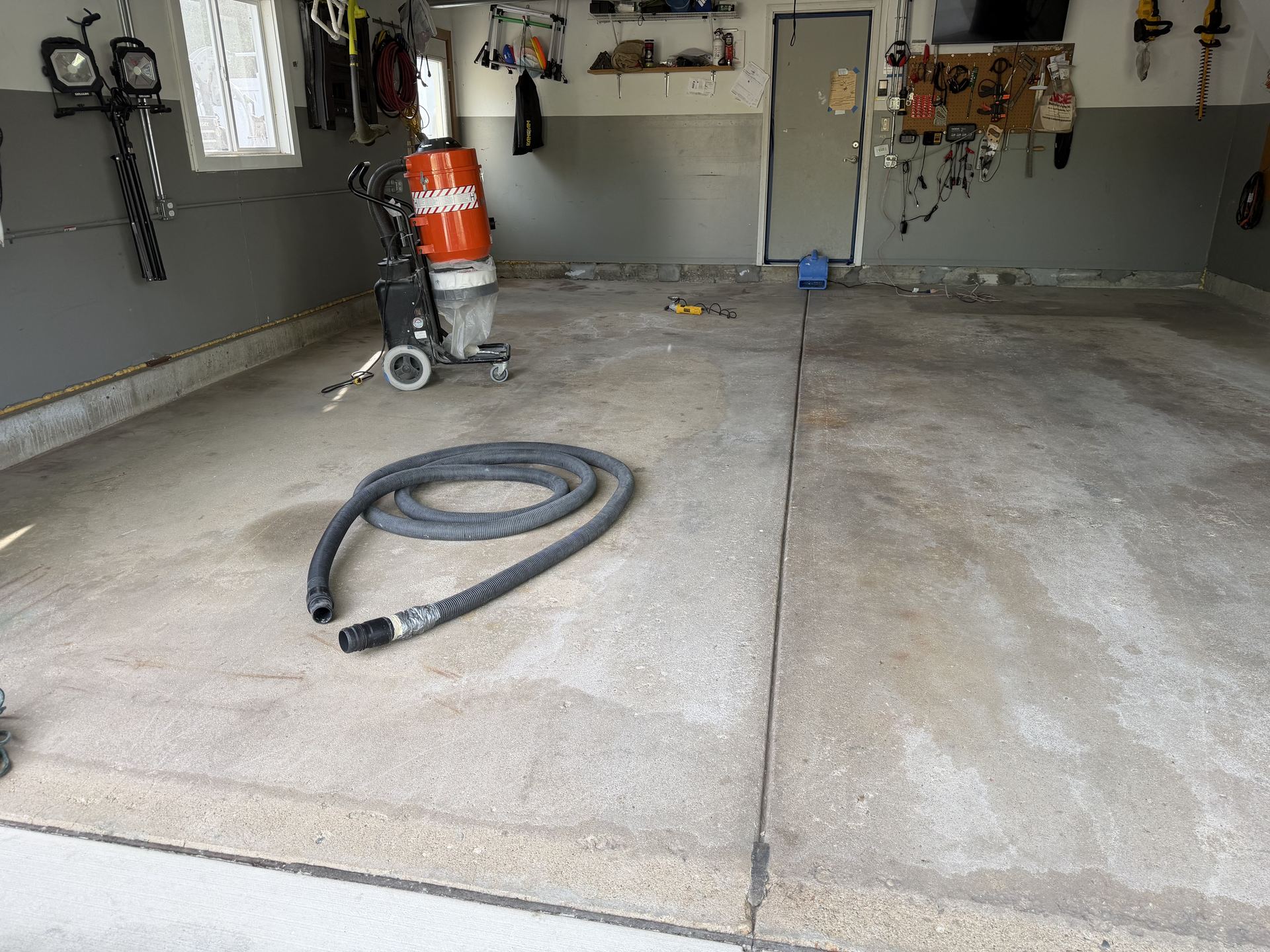 Empty garage with concrete floor, coiled black hose, and cleaning equipment near the back wall.